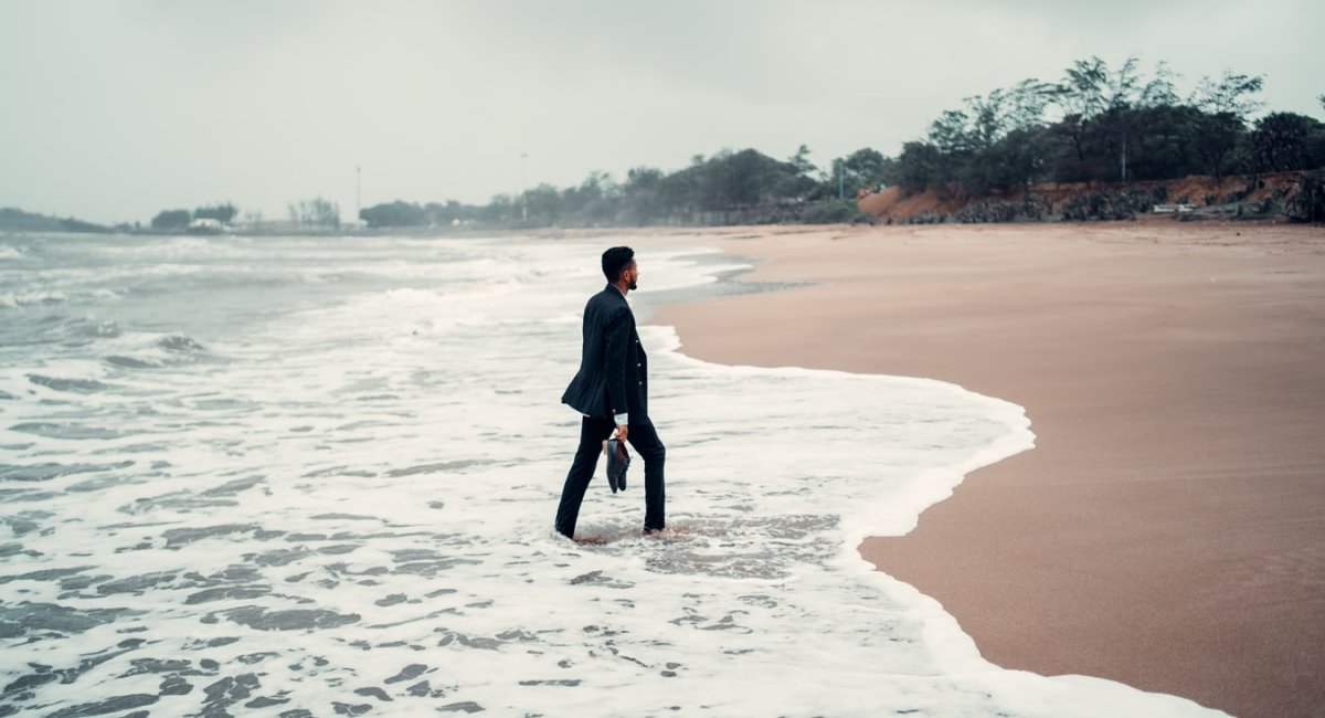 Would you wear a suit on a beach? Man in business suit walking on a beach